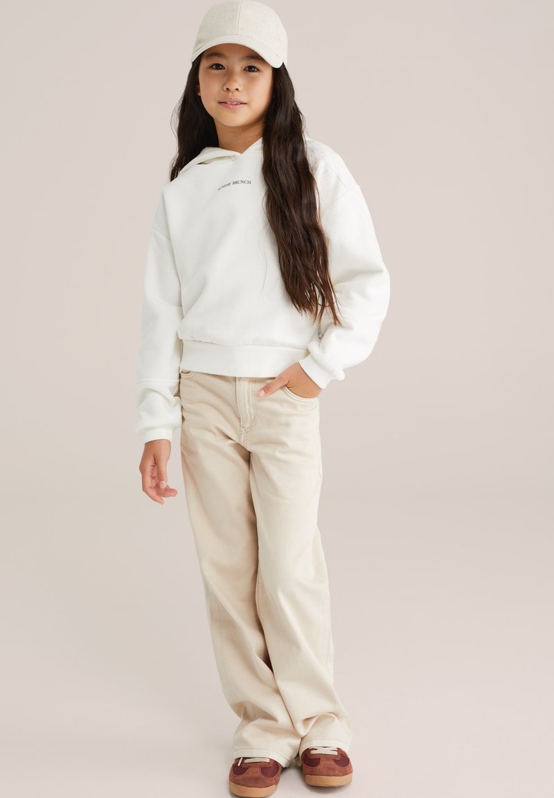 Felpa bianca con cappuccio recante la scritta "SUNDAY BRUNCH", abbinata a pantaloni beige a gamba larga e sneakers marroni. Cappellino da baseball color beige indossato.