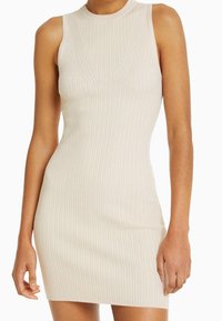 Robe ajustée à côtes en beige clair avec un col haut et sans manches. Présente des rayures verticales et une texture lisse.