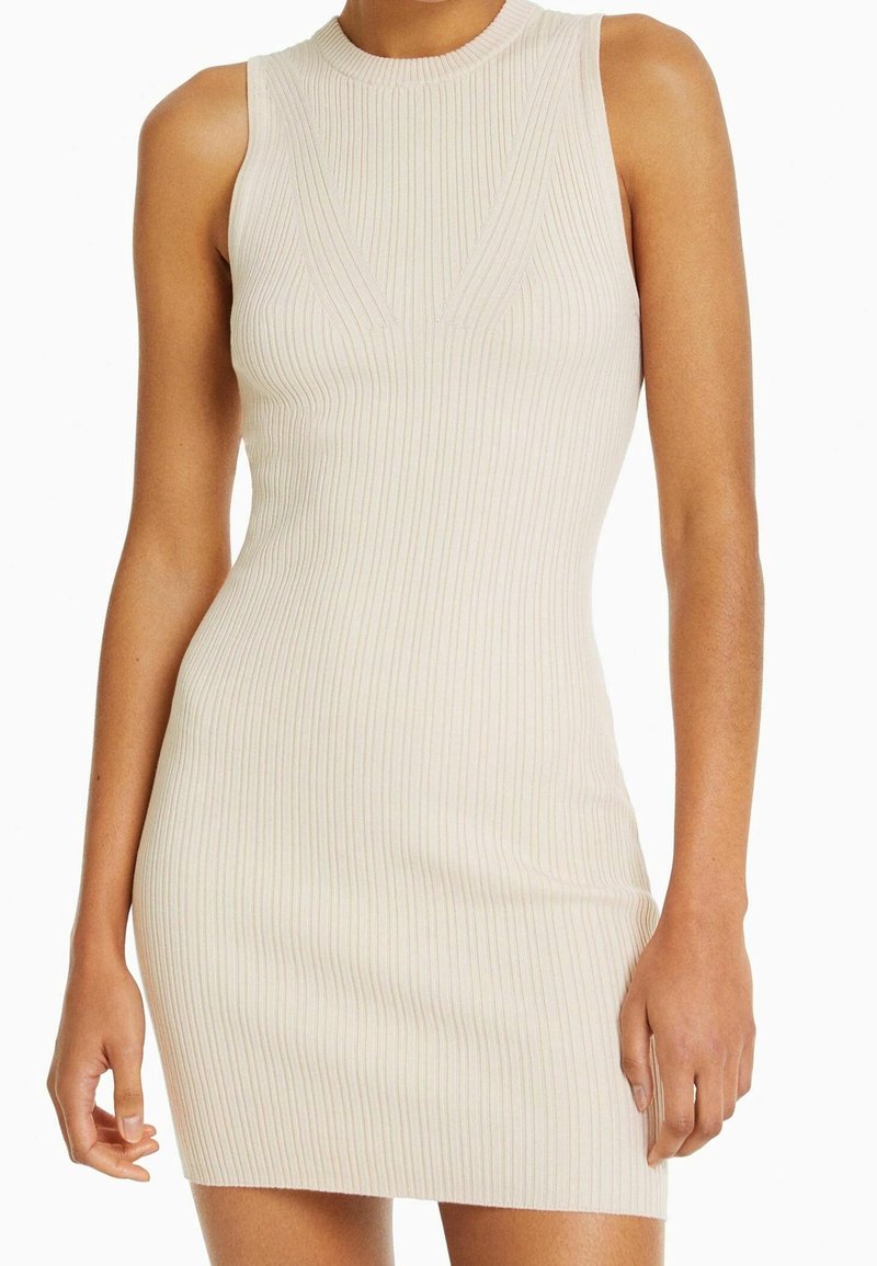 Robe ajustée à côtes en beige clair avec un col haut et sans manches. Présente des rayures verticales et une texture lisse.