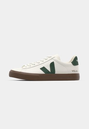 Vit sneaker med grön mocka V-logotyp, brun gummisula, rund tå och platta snören. Märkning på hälen och sidan i guld.