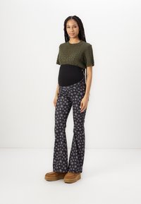 Un haut tricoté vert à manches courtes, un panneau noir au niveau du ventre, un pantalon évasé noir à motifs floraux, et des chaussures à plateforme marron.