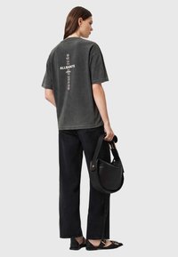 Grå oversized t-shirt med grafisk print på ryggen, sammen med sorte vide jeans og en lille sort lædertaske. Flade sko fuldender looket.