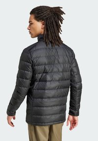 Svart pufferjakke med quiltet design, høy krage og lange ermer. Materialet ser blankt ut med en jevn tekstur.