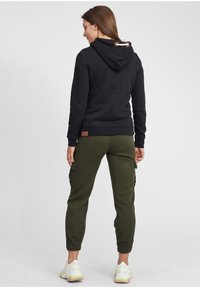 Felpa nera con cappuccio e cordino, abbinata a pantaloni cargo verde oliva con tasche laterali e polsini elasticizzati.