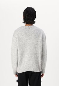 Maglione grigio a maglia con vestibilità ampia, dotato di scollatura a girocollo a coste e orlo posteriore leggermente più lungo. Texture morbida e pelosa.