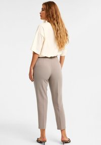 Vaalean kermaisen suureksi mitoitettu t-paita yhdistettynä muotoiltuihin vaaleanbeigeihin housuihin ja eläinkuosilla varustettuihin liukuvarvassandaaleihin. Pitkät, laineikkaat hiukset näkyvissä.