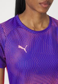 Gros plan d'une personne portant un maillot de sport Puma à motifs violets et roses, montrant la poitrine et la zone du cou.