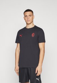 T-shirt nera a maniche corte realizzata in misto cotone, con un piccolo logo rosso Puma sul lato sinistro del petto e un emblema rosso del AC Milan sul davanti.