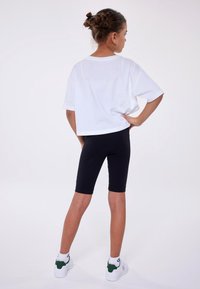 T-shirt bianco corto con maniche corte, abbinato a leggings neri alla ginocchio e sneaker bianche con dettagli verdi. Design semplice.