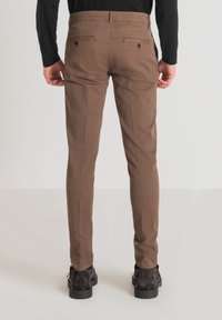 Pantalon marron ajusté avec une texture subtile, coupe slim et deux poches arrière. Porté avec des bottines noires pour un look complet.