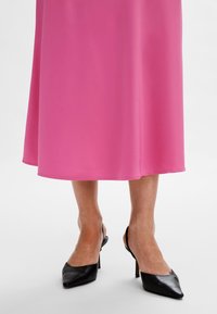 Vaaleanpunainen, liehuva midimekko pehmeästä, kevyestä kankaasta. Mustat kärjetön korkokengät, joissa on avonainen kantapää ja hoikat stiletto-korot.