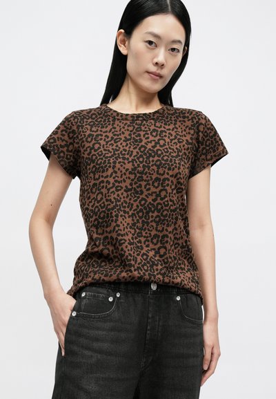 Brązowy T-shirt w panterkę z krótkim rękawem i okrągłym dekoltem, zestawiony z czarnymi denimowymi spodniami z przednimi kieszeniami i srebrnymi detalami.