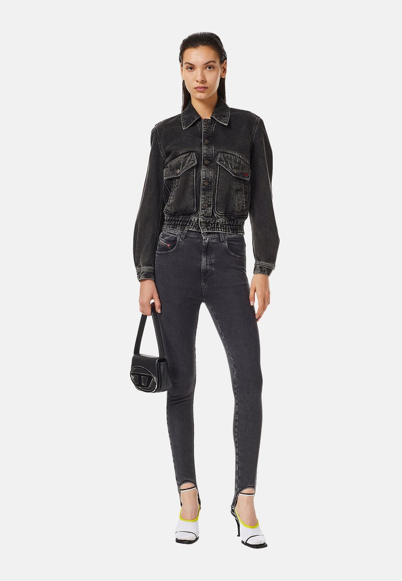 Giacca di jeans nera con tasche frontali, elastico in vita; abbinata a jeans neri a vita alta, completata con scarpe con tacco bianche e gialle.