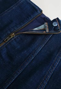 Ciemna kurtka dżinsowa z złotym zamkiem błyskawicznym, kontrastowymi przeszyciami i niebieską podszewką. Widoczne zapięcie na guziki oraz podwójne kieszenie.