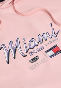 Tessuto rosa con testo "Miami 2026 1-3 maggio", logo Cadillac e logo della bandiera Tommy Hilfiger stampati sulla superficie.
