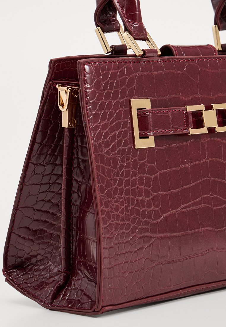 Sac à main en cuir bordeaux avec un motif crocodile texturé, quincaillerie en ton or, et une forme structurée. Présente des poignées supérieures doubles et un fermoir.