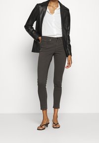 Jeans ajustados de color gris oscuro con una textura suave, con un corte slim y dobladillo deshilachado, combinados con una camisa blanca y una americana de cuero negra.