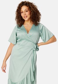 Mintgroene satijnen wikkeljurk met korte mouwen, v-hals, strikdetail om de taille en een vloeiende rok. Gladde textuur en elegante drape.