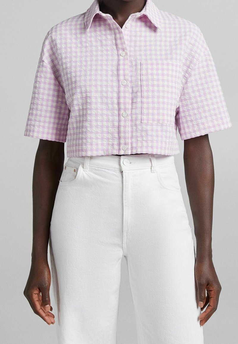 Kortsärmad skjorta med ljuslila rutigt mönster, med framsidig bröstficka, i kombination med högmidjade vita byxor.