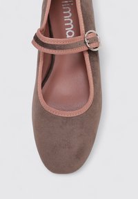 Zapato plano tipo Mary Jane en ante marrón con un borde rosa, que presenta una puntera redonda y una correa con un detalle de hebilla plateada.