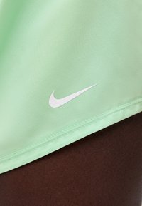 Ανοιχτό πράσινο ύφασμα με το λευκό λογότυπο Nike swoosh κοντά στο ραμμένο στρίφωμα σε σκούρο καφέ φόντο δέρματος.