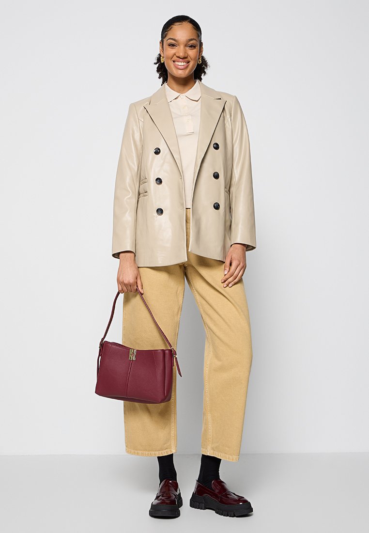 Beige Leder Doppelreiher-Blazer, hellfarbiges Hemd, lässige beige Hose, kastanienbraune Handtasche, polierte Schuhe mit schwarzen Sohlen.