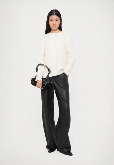 Cream sweater with a round neckline and bow detail, paired with high-waisted black leather wide-leg trousers and a small black handbag.
