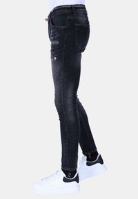 Dunne zwarte spijkerbroek met versleten details, een vijf-pocket ontwerp en een donkere wassing. Gecombineerd met witte sneakers met zwarte accenten.