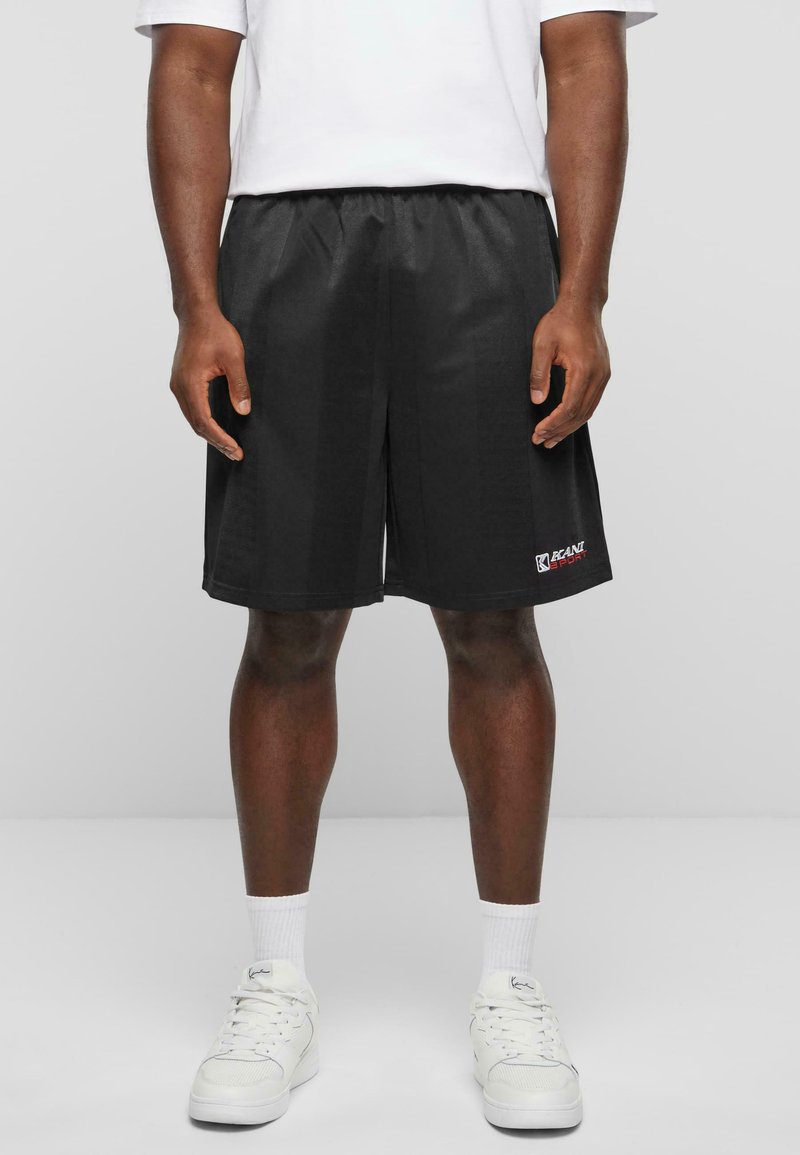 Shorts de sport noirs avec une taille élastique, fabriqués en tissu lisse. Présentent un petit logo rouge en bas à gauche.