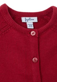 Roter gestrickter Baby-Pullover mit runder Ausschnittlinie, ausgestattet mit einer vorderen Knopfleiste, zwei runden rosa Knöpfen und einer weichen Textur. Markenetikett sichtbar.