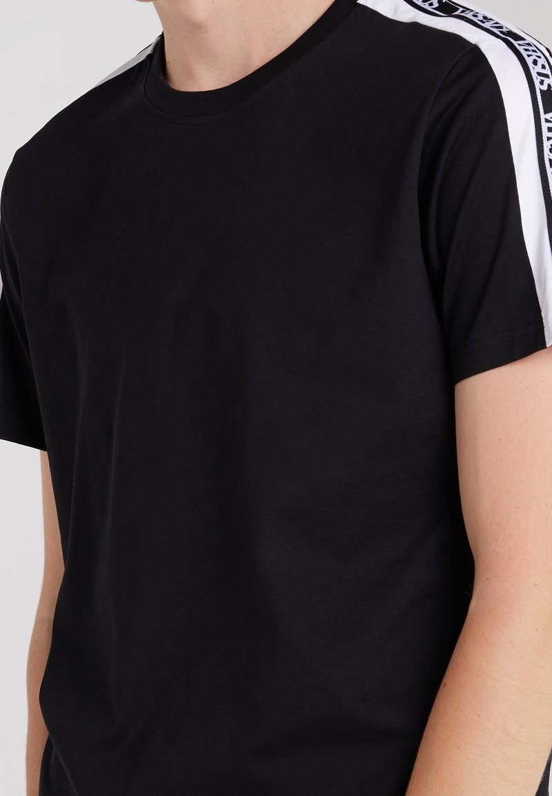 T-shirt noir à manches courtes avec des bandes blanches et noires à motifs le long des épaules et des bras supérieurs.