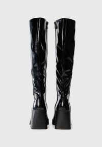 Black knee-high boots made of glossy material. Square heels with a ribbed texture. Zipper detail on the side, smooth silhouette.