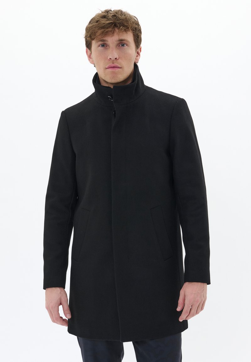 Manteau noir en mélange de laine avec un col haut, des poches avant et une silhouette droite. Texture lisse, design minimal et fermeture à boutons.