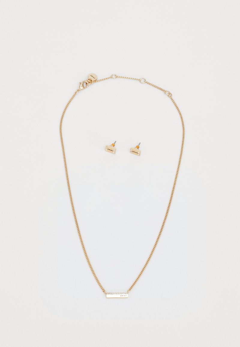 Collana di tonalità oro con una catena sottile e un ciondolo rettangolare. Orecchini a perno abbinati presentano piccole forme rettangolari con intagli decorativi.