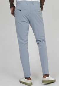 Světle modré kalhoty vyrobené z texturované látky, se dvěma zadními kapsami na knoflíky. Nošeny s bílými teniskami a ohrnutými manžetami.