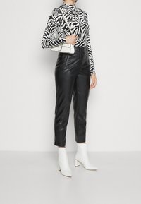 Svarta läderbyxor med hög midja i kombination med en långärmad topp med svart-vitt zebramönster. Vita anklarboots fulländar looken.