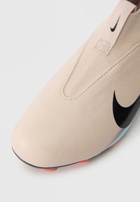 Nike futbola apavi gaiši bēšā krāsā ar teksturētu virsmu, melnu swoosh logotipu un oranžiem akcentiem uz zoles. Gluds, viegli uzvelkams dizains.