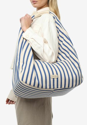 Gestreepte canvas tas in blauw en crème, met een ruime indeling, zachte textuur en een logo-label aan de voorkant.