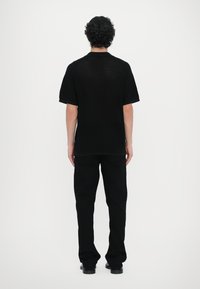 Juodas megztinis trumpomis rankovėmis su apykakle, derinamas su juodomis tiesiomis kelnėmis. Audinys rodo tekstūrą su subtiliu raštu.