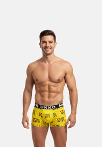 Boxers amarillos con una cinturilla negra que presenta texto y patrones gráficos. El material parece suave y elástico, diseñado para la comodidad.