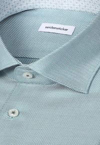 Chemise habillée texturée vert clair avec des boutons blancs et une étiquette blanche à l'intérieur du col indiquant "seidensticker."