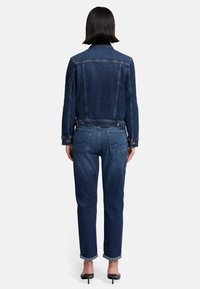 Giubbotto in denim scuro con un design aderente, dotato di colletto, polsini con bottone e chiusura a doppio bottone. Abbinato a jeans scuri a gamba affusolata.