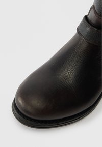 Juodo odinio kulkšnies bato su apvalia nosimi, tekstūruotu paviršiumi ir siūta padu, užtikrinančiu patvarumą. Išskirtinai elegantiškas dizainas su minimaliais akcentais.