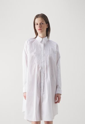 Rochie albă din bumbac, cu un design plisat, decolteu cu nasturi și accesorii subtile, având o croială lejeră, supradimensionată.