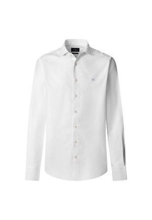 Camisa blanca de manga larga hecha de algodón. Presenta un cierre frontal con botones, cuello clásico y un sutil logotipo azul en el pecho. Textura suave.