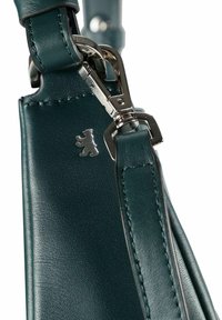 Correa de bolsa de cuero verde oscuro con broche de metal plateado y pequeño logotipo de oso plateado grabado en el cuero cerca del punto de sujeción.