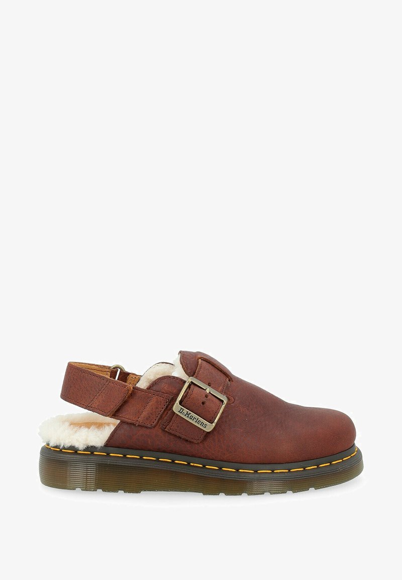 Bruine leren schoen met een gespband, pluizige witte voering en een rubberen zool. Heeft gele stiksels langs de rand van de zool.