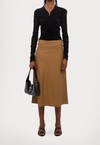 Mustat rypytetyt pitkähihaiset paidat, beige midi-hame, mustat korkokengät ja pieni musta käsilaukku, jossa on hopeiset yksityiskohdat.