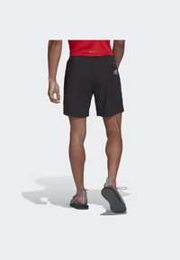 Pantaloni sportivi neri con elastico in vita e un logo bianco sul lato sinistro, abbinati a sandali sportivi grigi e arancioni.