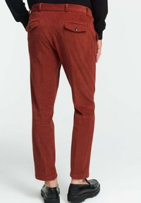 Baumwollcordura-Hosen in verbranntem Orange mit figurbetontem Schnitt, ausgestattet mit Gesäßtaschen mit Knöpfen und einer glatten Textur.